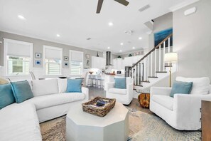 A modern living room with white sofas, a coffee table, and a staircase leading to a kitchen. - Sea Mist by Stay on 30a (Inlet Beach)