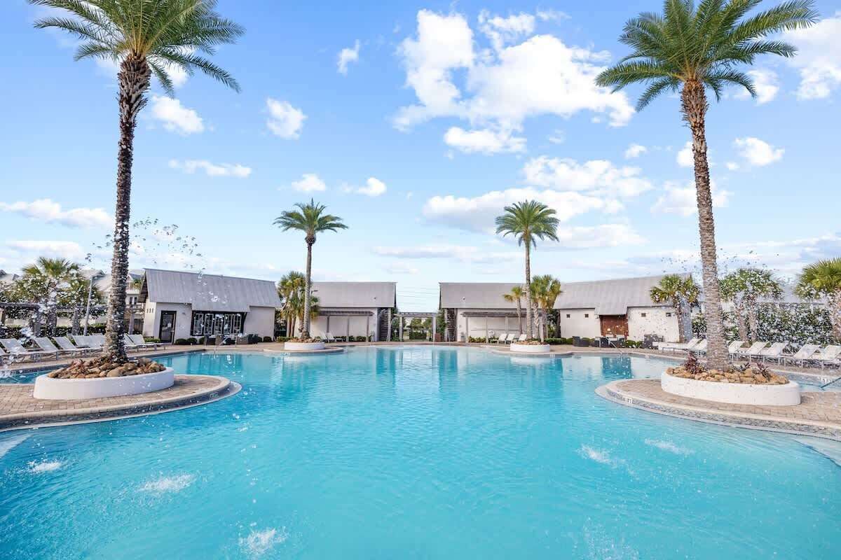 A swimming pool with palm trees, lounge chairs, and a building with a grey roof.