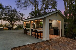 A covered outdoor area with a bar and seating, surrounded by trees. - Waterfront - Pool - Pickleball - Basket -Sleeps 18 (Westchase)