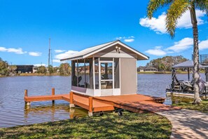 A small docked cabin with a glass enclosure, a wooden deck, and a gazebo in the background. - Waterfront - Pool - Pickleball - Basket -Sleeps 18 (Westchase)
