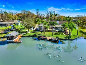 A lakeside property with a dock, a covered boat house, and a swimming pool surrounded by lush greenery and palm trees. - Waterfront - Pool - Pickleball - Basket -Sleeps 18 (Westchase)