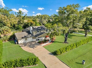 A two-story house with a driveway leading to the garage, surrounded by a well-maintained lawn and mature trees.