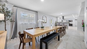 Eine moderne Küche mit weißen Schränken, einer zentralen Kochinsel und einem Essbereich mit Holztisch und Stühlen.