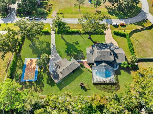 A residential property with a swimming pool, tennis court, and a large house with a unique roof design.