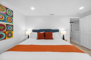 A hotel room with a large bed, two bedside lamps, a colorful abstract painting on the wall, and a white door. - Private Pool - Pickleball - Game Room - Sleeps 18! (Westchase)