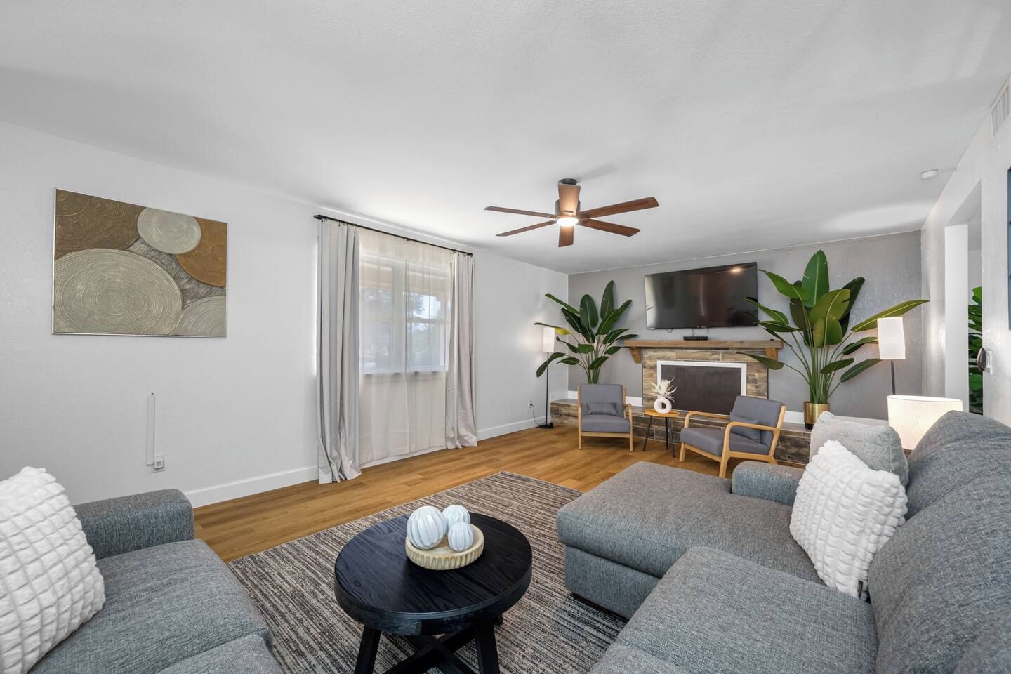 Un salon moderne avec des canapés gris, une table basse noire et un ventilateur de plafond.
