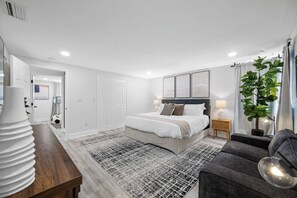 A modern bedroom with a large bed, bedside tables, a grey sofa, and a potted plant.