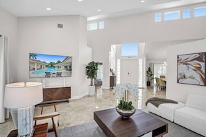 A spacious living area with a flat-screen TV, a dining table, and a sofa. - The Grand Luxe 8Br Villa w Pool and Basketball (Pembroke Pines)