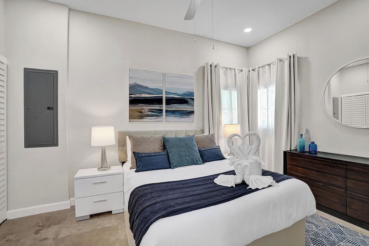 A modern bedroom with a bed, bedside tables, a dresser, a mirror, and a painting on the wall.