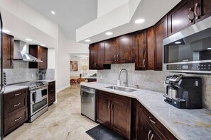 A modern kitchen with dark wood cabinets, stainless steel appliances, and a marble countertop. - The Grand Luxe 8Br Villa w Pool and Basketball (Pembroke Pines)