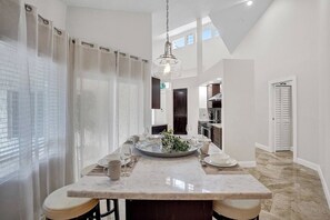 Una cocina moderna con una isla central, iluminación colgante y vistas al área de comedor contigua.