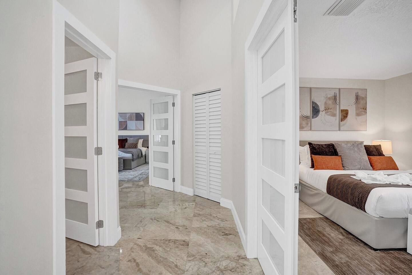 A hallway leading to a bedroom with a bed, a closet, and a door with frosted glass panels.