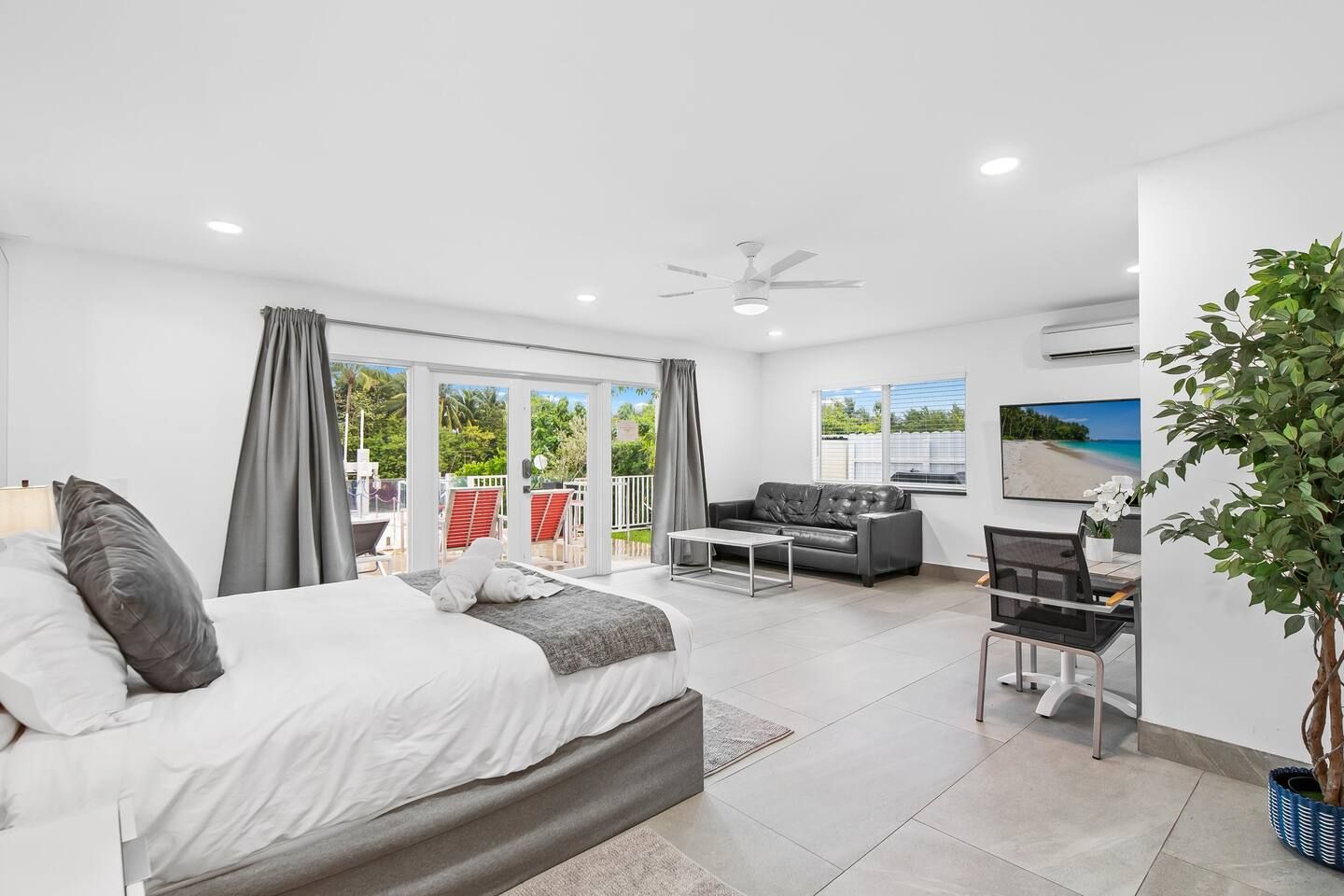 A modern hotel room with a bed, a desk, a sofa, and a balcony with outdoor furniture.