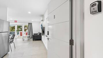 A modern hotel room with a kitchenette, a sofa, a flat-screen TV, and a door with a security lock.