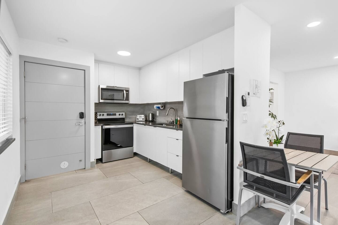 A modern kitchen with white cabinets, stainless steel appliances, and a dining area with a table and chairs.