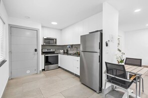 Une cuisine moderne avec des meubles blancs, des appareils en acier inoxydable et un coin repas comprenant une table et des chaises.