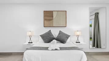 A modern bedroom with a large bed, two bedside tables, a wall-mounted artwork, and a view through a window with curtains.