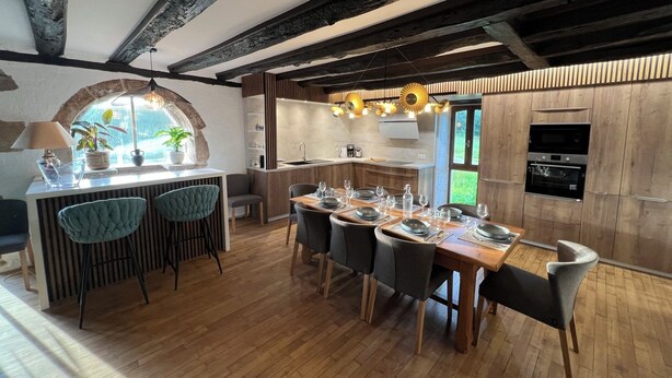 Une cuisine moderne avec des meubles en bois, un four encastré et un coin repas comprenant une table et des chaises en bois.
