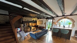 Un intérieur rustique avec un escalier en bois, une cheminée en pierre, un canapé bleu et un coin bar avec des tabourets.