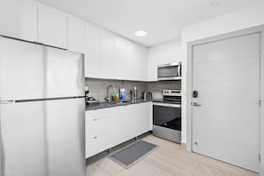A modern kitchen with white cabinets, a stainless steel refrigerator, a microwave, a toaster, and an oven. - Spacious Apartment w/Patio & Mini-Golf (Deerfield Beach)