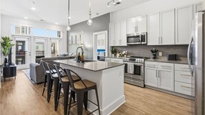 Una cocina moderna con armarios blancos, electrodomésticos de acero inoxidable y una isla central con taburetes de bar.