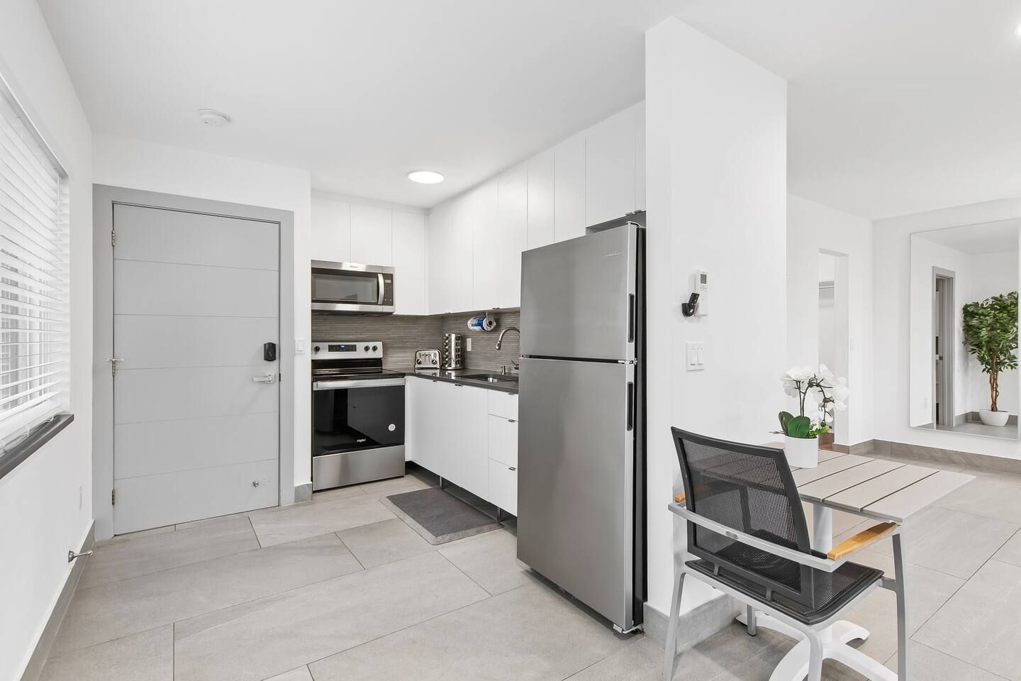 A modern kitchen with stainless steel appliances, a dining area with a chair and table, and a potted plant.