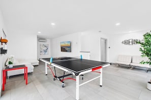 Et moderne værelse med et ping pong bord, en hvid sofa, et rødt bord og en plante.