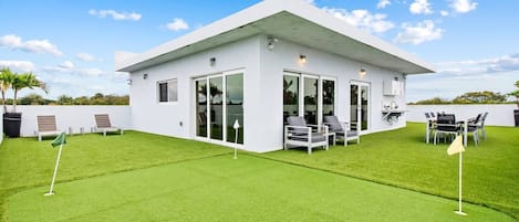 Un edificio moderno con techo plano, grandes puertas de vidrio y un patio con mobiliario exterior.