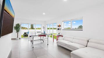 Una sala de estar moderna con un sofá blanco, una mesa de comedor y un amplio ventanal con vistas al exterior.
