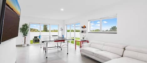 Un salon moderne avec un canapé blanc, une table à manger et une grande fenêtre donnant sur l’extérieur.