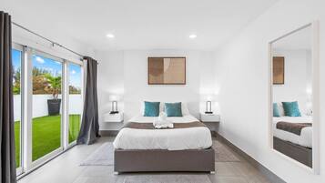 Un dormitorio moderno con una cama grande, dos mesitas de noche, un espejo y vistas a un césped verde a través de puertas correderas de vidrio.