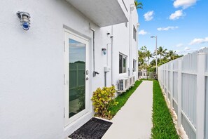 A white building with a pathway leading to the entrance, air conditioning units, and a small garden area. - Apt w/Patio, Balcony & Mini-Golf (Deerfield Beach)
