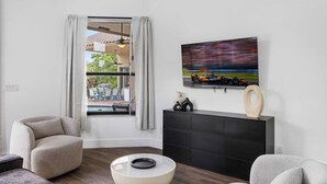 Ein modernes Wohnzimmer mit an der Wand montiertem Fernseher, einer schwarzen Unterhaltungsanlage und Blick auf eine Terrasse.