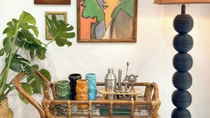 Una stanza con un tavolino in legno, una pianta in vaso, un quadro incorniciato e una lampada.