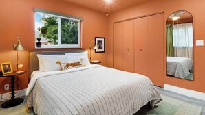 Una camera da letto con un letto, una finestra con piante, uno specchio e una ventola a soffitto.