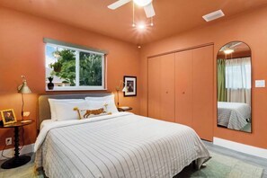 A bedroom with a bed, a window with plants, a mirror, and a ceiling fan. - 5 min to beach w/pool & BBQ (Fort Lauderdale)