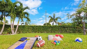 Un'area verde con attrezzature sportive, tra cui un pallone da calcio, un pallone da football e palloni da pallavolo, e un percorso ad ostacoli in legno.