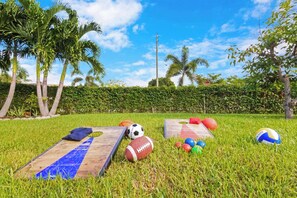 A grassy outdoor area with sports equipment, including a soccer ball, football, and volleyballs, and a wooden obstacle course. - 5 min to beach w/pool & BBQ (Fort Lauderdale)
