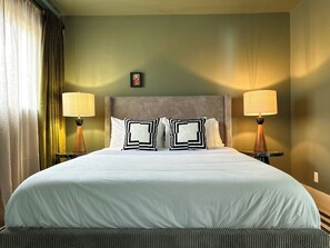 Ein Hotelzimmer mit einem großen Bett, zwei Nachttischlampen, einem Kopfteil und einem gerahmten Bild an der Wand.