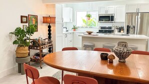 Una cucina moderna con mobili bianchi, un'isola centrale e una zona pranzo con tavolo in legno e sedie rosse.