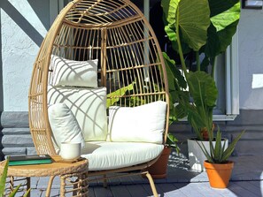A wicker chair with cushions, a small table with a book and a cup, and potted plants. - 5 min to beach w/pool & BBQ (Fort Lauderdale)