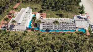 An aerial view of a resort with multiple swimming pools, a large building with balconies, and palm trees surrounding the area. - The Grand Resort, Rarotonga (Rarotonga)
