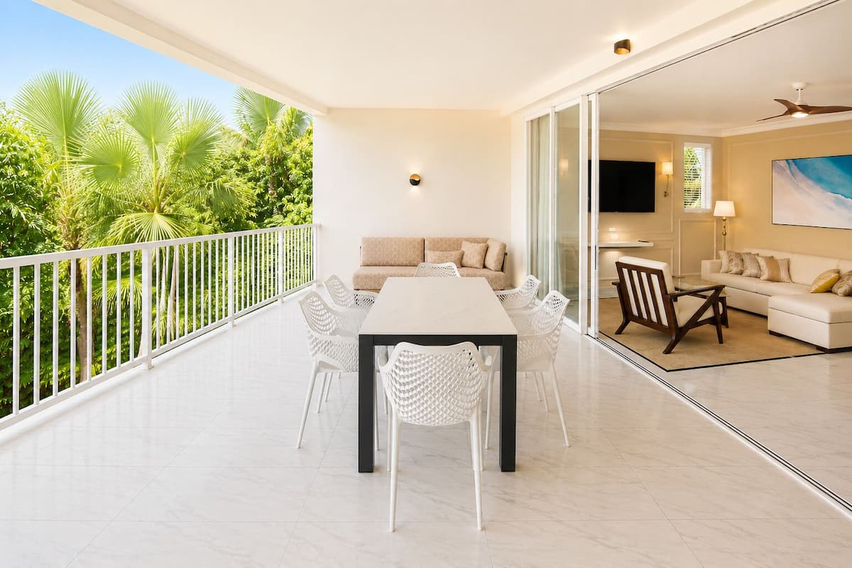 A balcony with a dining table and chairs, a sofa, and a TV in a living area.
