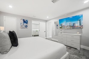 A bedroom with a large bed, a dresser, a mirror, and a cityscape painting on the wall.