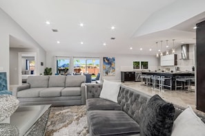 A modern living room with a grey sofa, a tufted armchair, and a dining area with a bar.