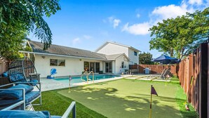 En baghave med swimmingpool, græsplæne og putting green, samt et træhegn.