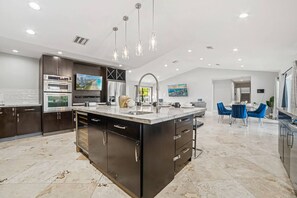 A modern kitchen with a central island, stainless steel appliances, and pendant lighting. - Heated Pool - Putting Green - 5 min from Beach! (Deerfield Beach)