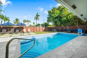 A swimming pool with a wooden deck, lounge chairs, and umbrellas. - Heated Pool - Putting Green - 5 min from Beach! (Deerfield Beach)