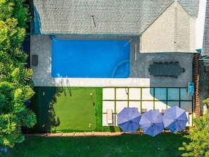A residential property with a swimming pool, a patio area with umbrellas, and a well-maintained lawn.