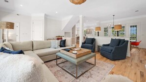 Ein modernes Wohnzimmer mit Sofa, Sessel, Couchtisch und einem Essbereich mit Tisch und Stühlen.